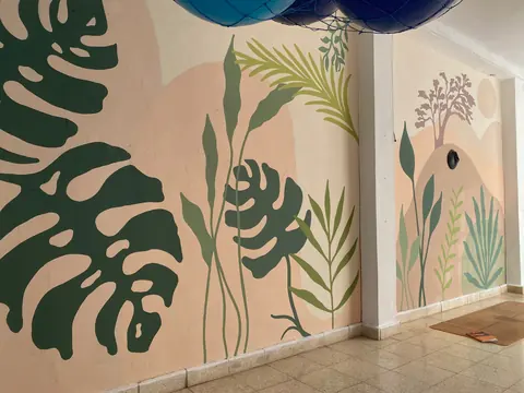 El mural del salón de yoga: monsteras, palmas y hojas verdes sobre soles durazno