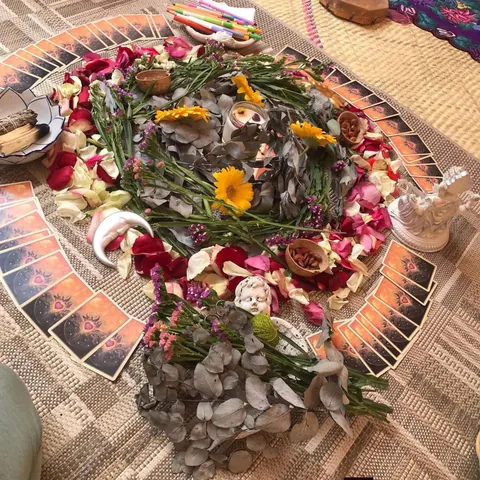Un altar en forma de mandala: flores, eucalipto, velas y cartas acomodadas en círculo sobre un tapete