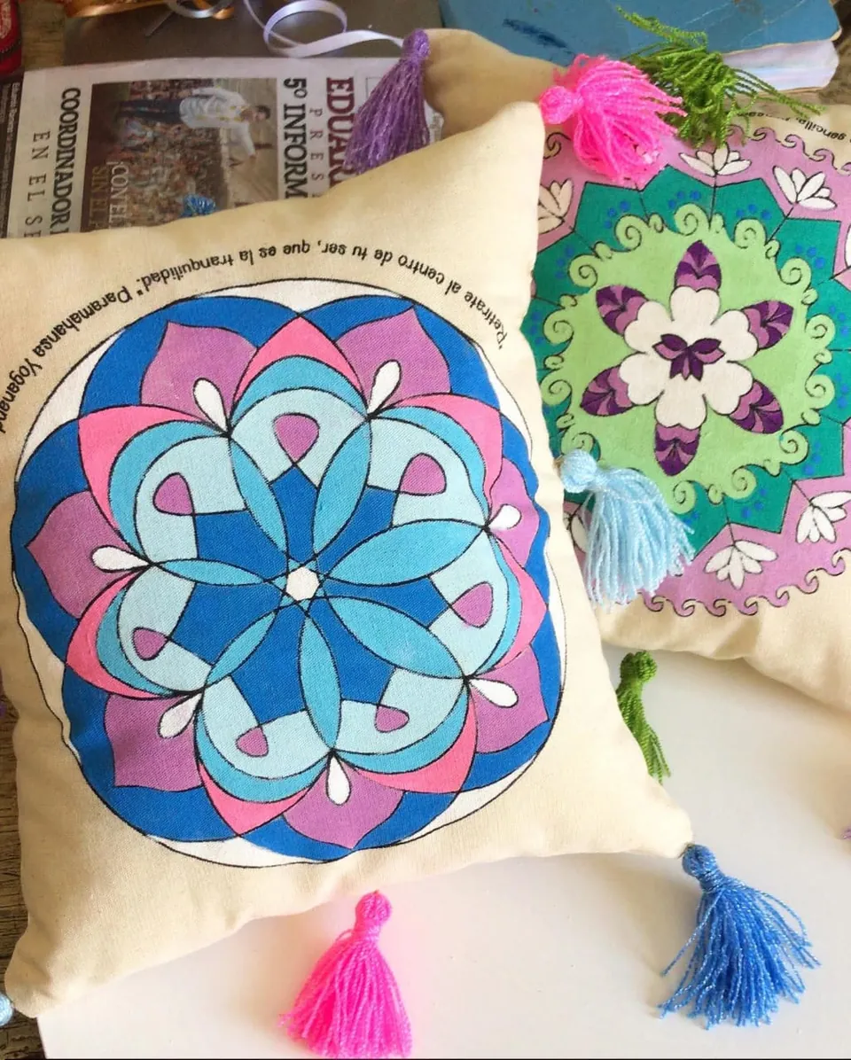 Dos cojines pintados con mandalas en azul, rosa y verde, con borlas de colores